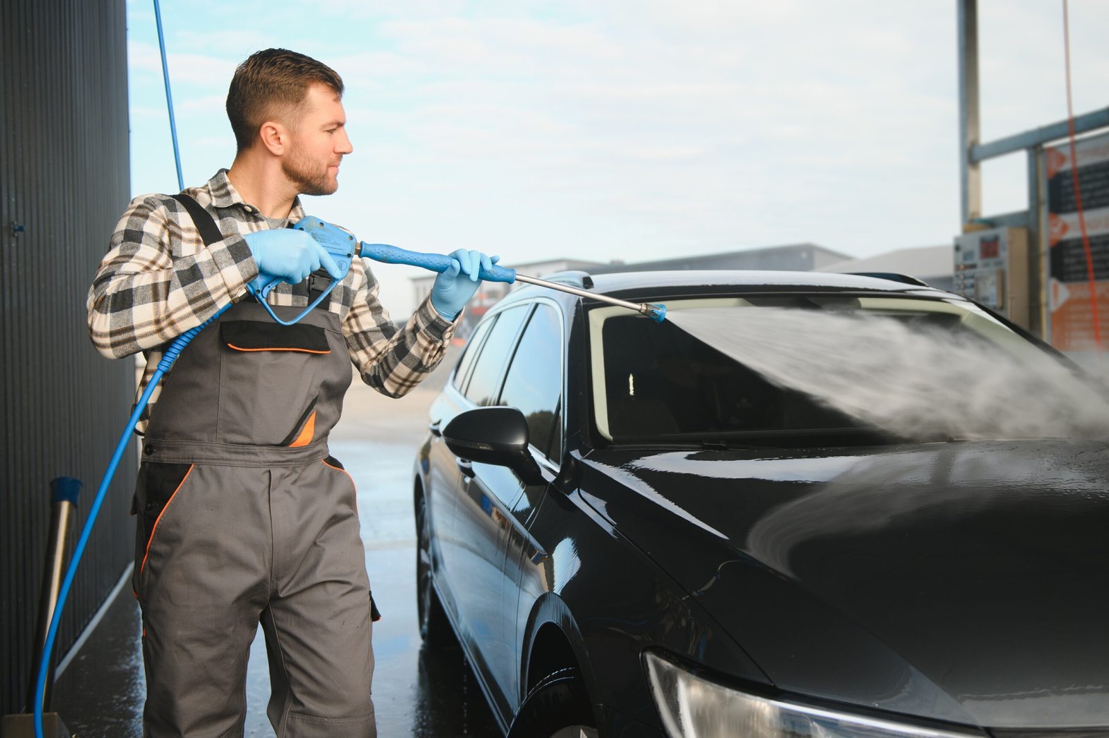 A car wash worker is using high pressure water gun for car washing.