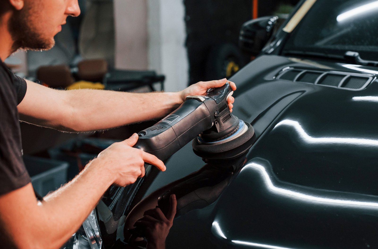 Guy polishing surface of vehicle. Modern black automobile get cleaned by man inside of car wash station.