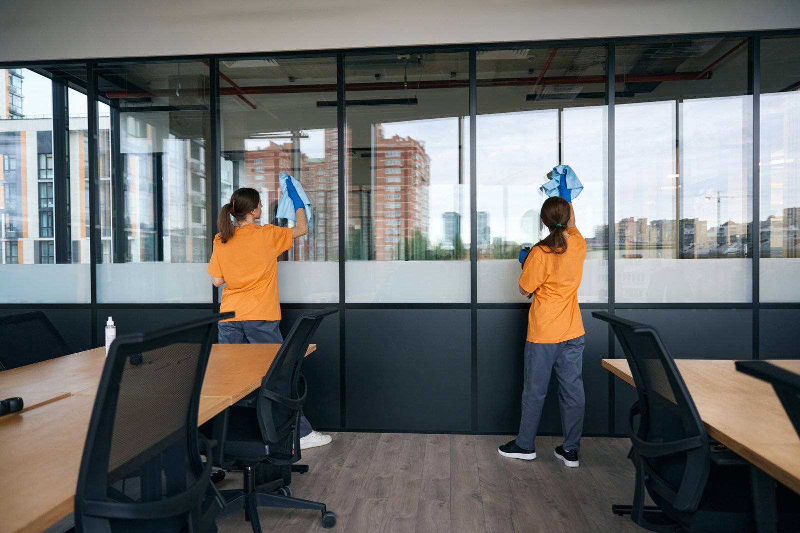 Two female employees of a cleaning company washing windows in a coworking space with a special product in protective gloves